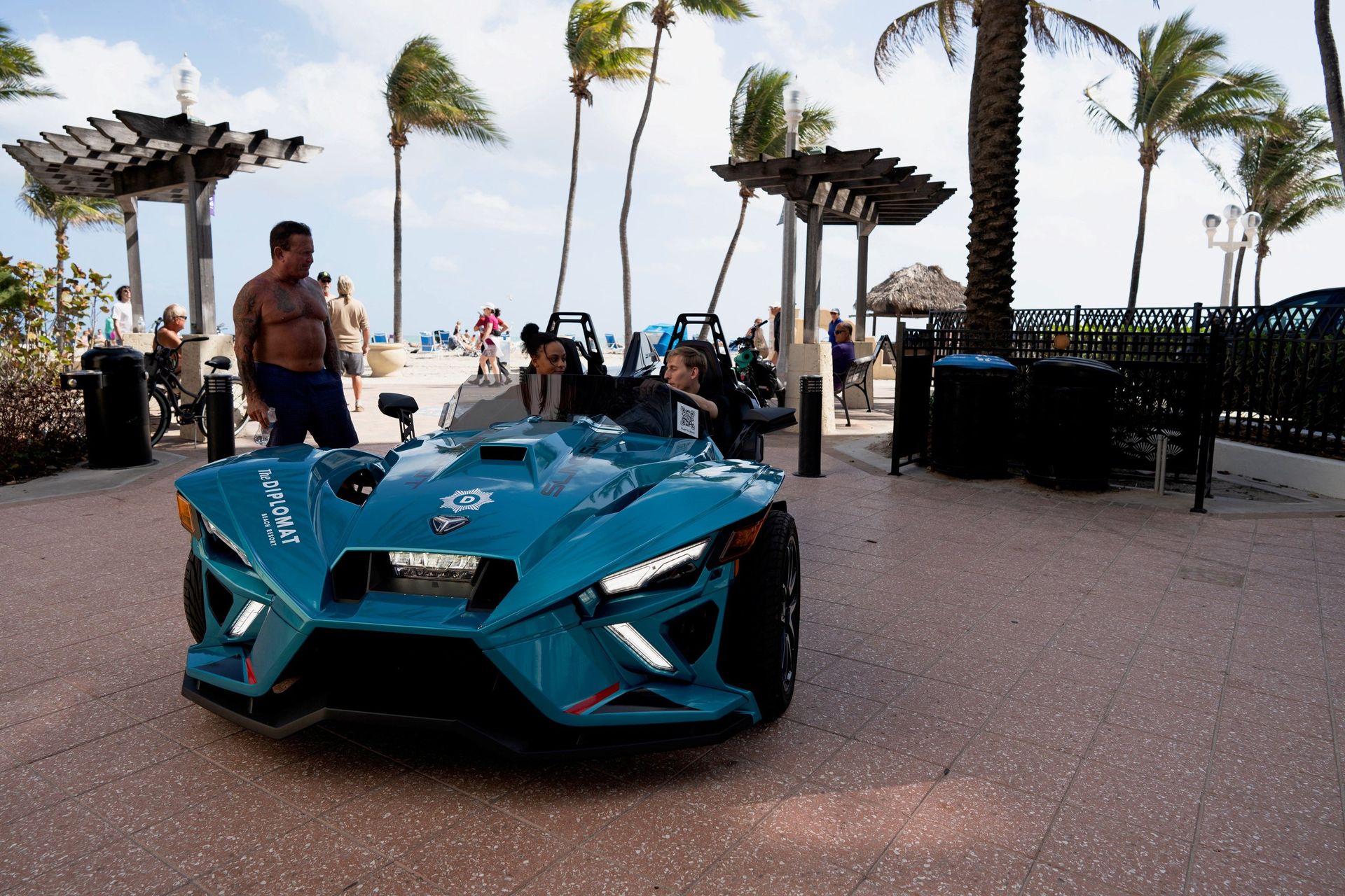 A teal Polaris Slingshot parked beside the Hollywood Beach Broadwalk