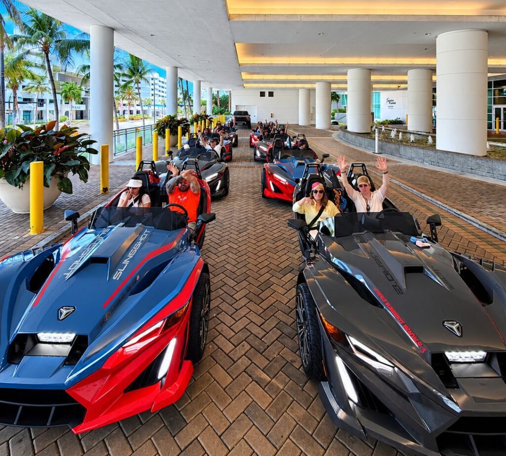 A convoy of red and black Polaris Slingshots with riders under the Diplomat Beach Resort entrance in Hollywood Beach